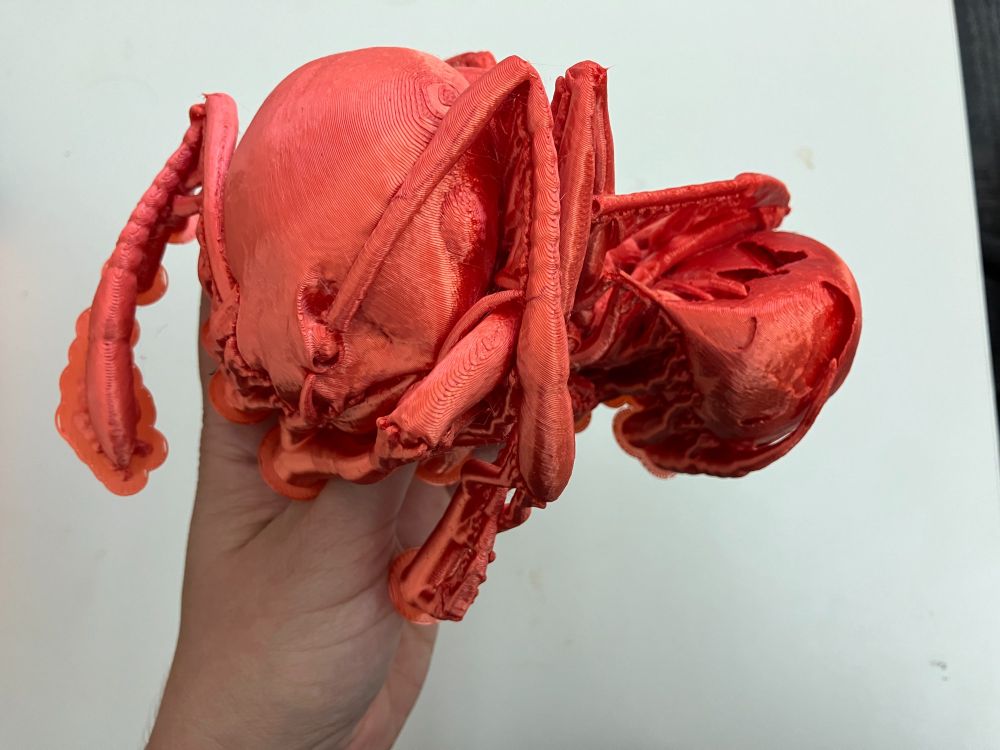 A 3D printed fire in red PLA being held, printing supports are still attached. 