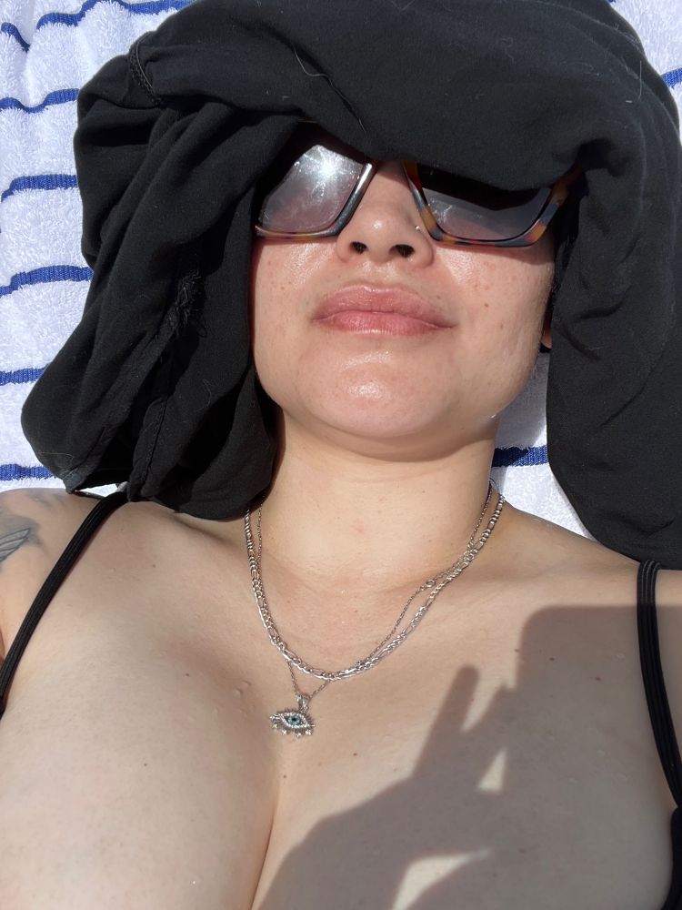 Jess laying on a beach chair with a black shirt covering half her face because she forgot a hat