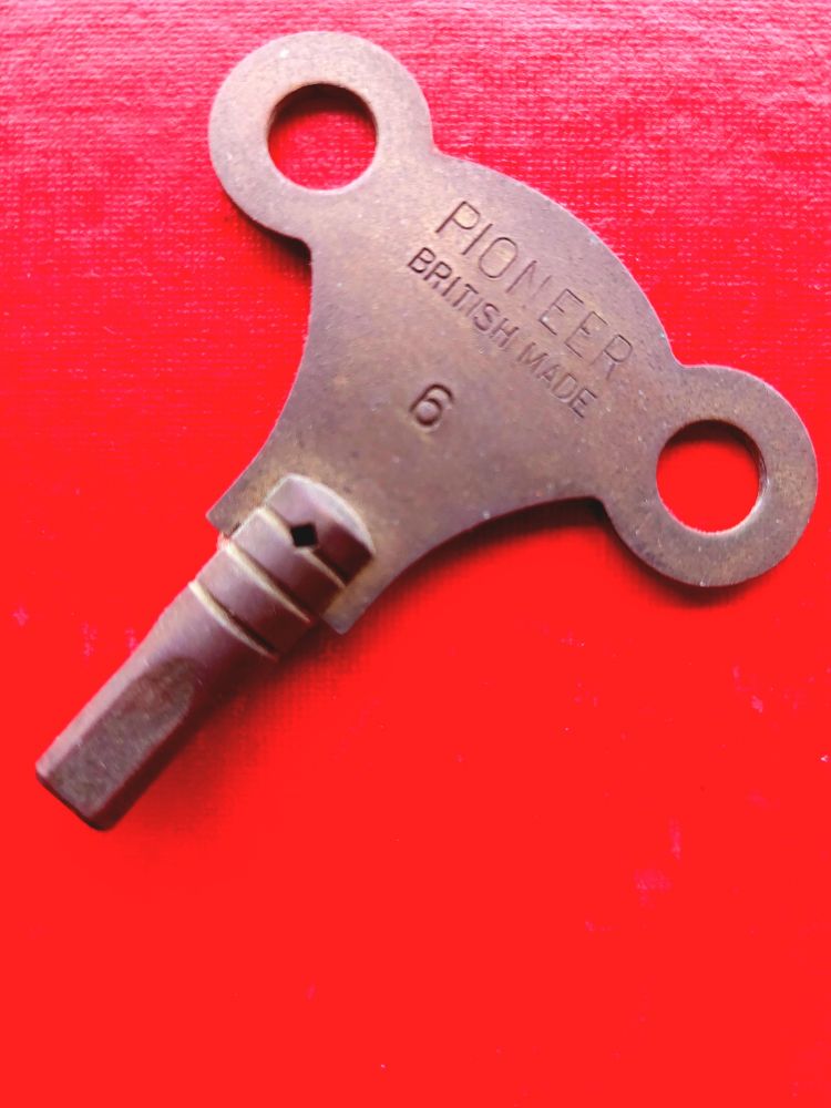 Ein Uhrenschlüssel aus Messing, etwa 2 cm breit, Vierkant in Größe 6 liegt auf rotem Untergrund. Er ist oben beschriftet mit PIONEER  British Made 6.