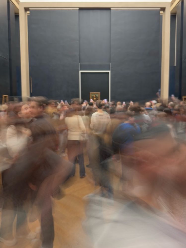 A large room with a large crowd in blurred motion staring at a small painting on a black wall. That painting is the Mona Lisa 