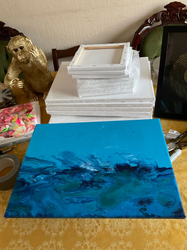 A painting that looks like a very rough sea being whipped up by the wind, under a blue sky. Various blues from dark to light swirl amongst greens and white. In the background is a pile of blank canvases and to the left is what looks like another small canvas wil multicolour swirl patterns on it. Behind that is a golden chimpanzee flipping off someone out of shot. 