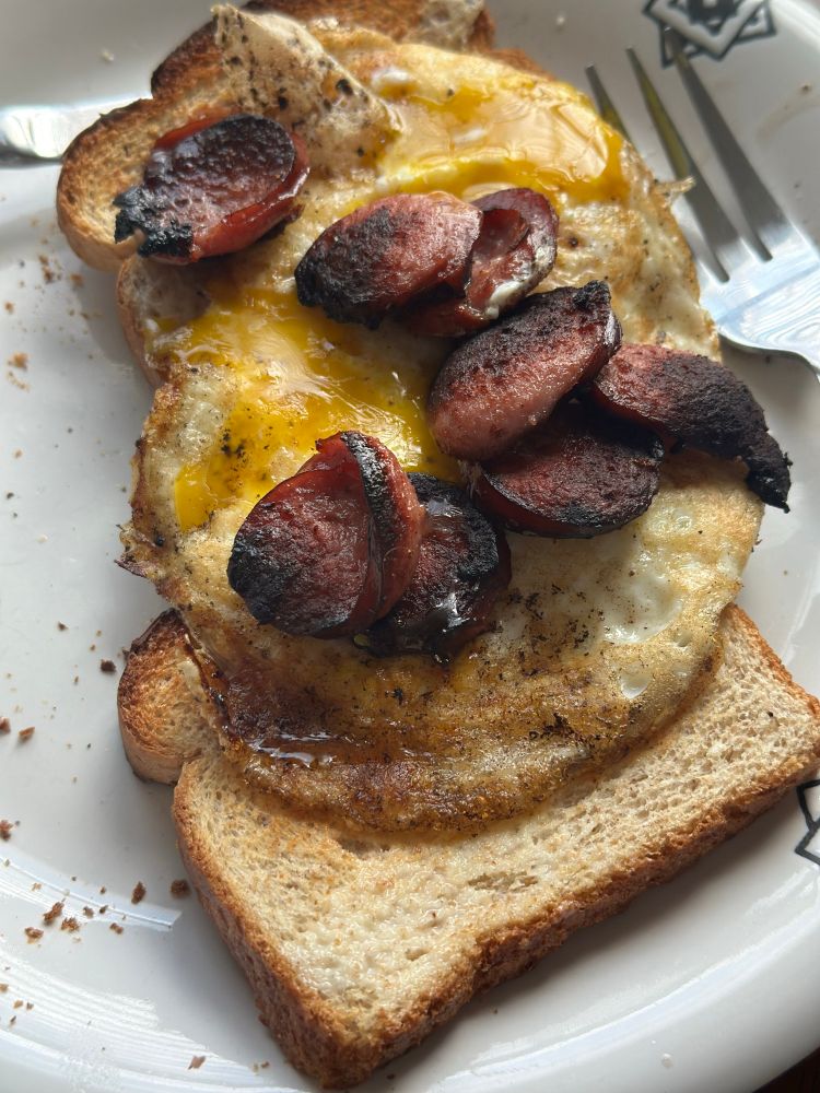 Runny eggs and beef sausage on toast placed on a white plate 