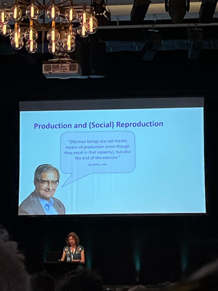 Keynote speaker Elise van Nederveen Meerkerk in front of a presentation slide showing Amartya Sen on production and social reproduction.