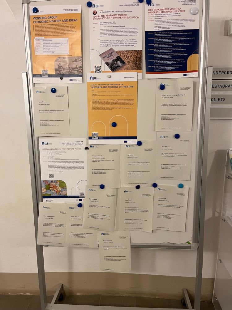 A whiteboard covered in posters advertising seminars and announcing upcoming PhD defenses.