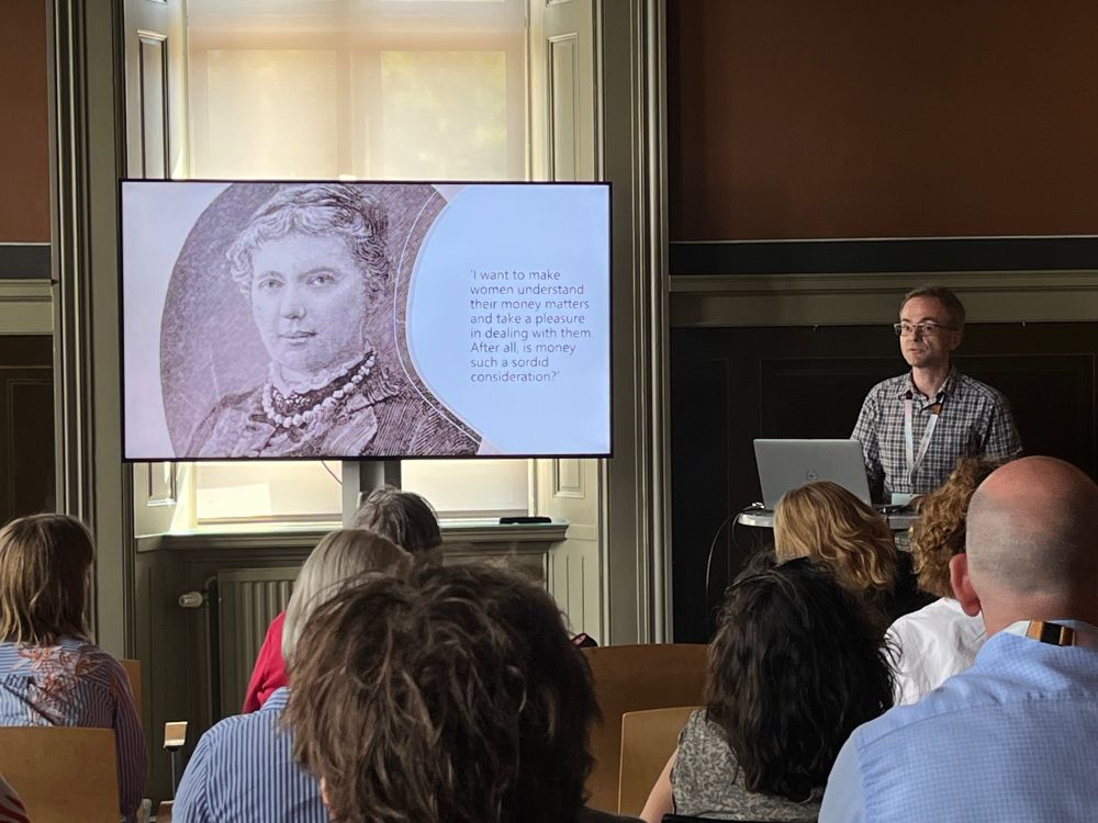 James Taylor presenting the work of female stockbrokers in nineteenth-century Britain, next to a slide showing Amy Bell defending women’s interest in finance, stating “I want to make women understand their money matters, and take a pleasure in dealing with them. After all, is money such a sordid consideration?”