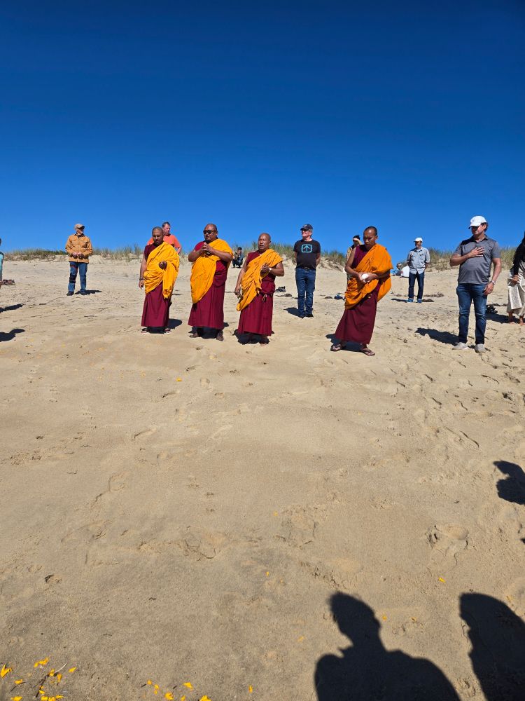 4 Buddist monks on the beach. Now their faces can be seen. Marigold petals are i the foreground where they were scattered in the ocean and habd been carried back ashore.