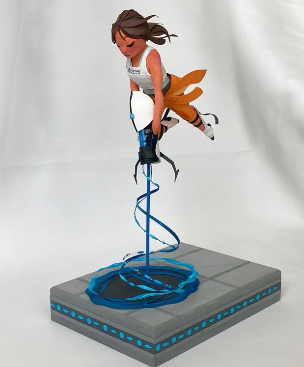 Paper sculpture of Chell from the video game portal. She’s flying thru the air, shooting a portal into the floor below her. 