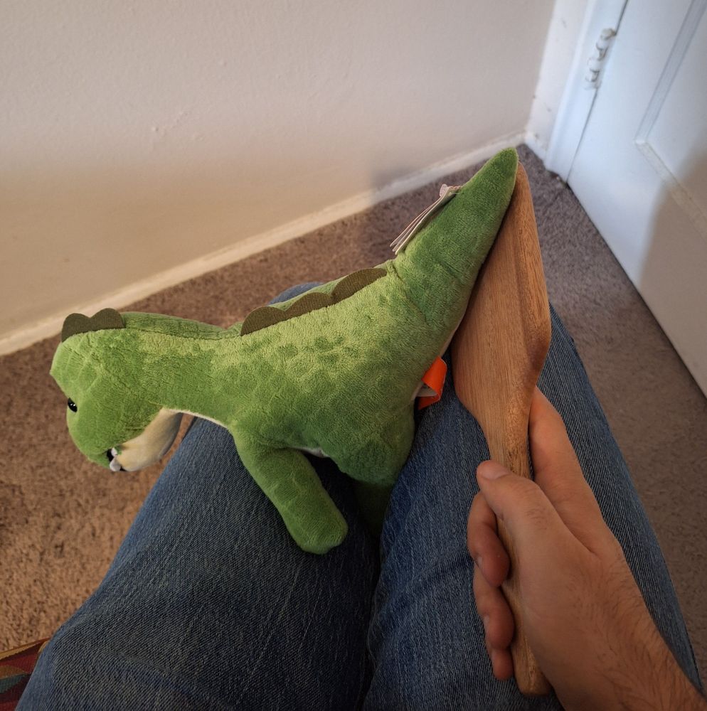 A small stuffed dinosaur getting its tail paddled over a human lap