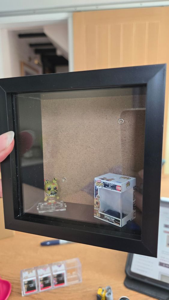 A 4x4 inch black shadow box frame containing a small, Springtrap Bitty Pop and its box