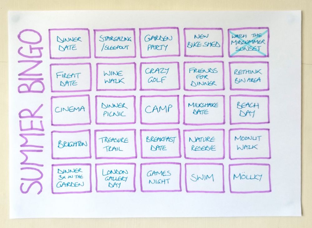 Hand-drawn bingo card on the wall, titled SUMMER BINGO to one side. Squares include 'watch midsummer sunset' (already crossed through), 'camp', 'swim', 'dinner picnic', 'crazy golf', 'treasure trail', 'garden party', 'games night', 'friends for dinner', 'beach day' and more.