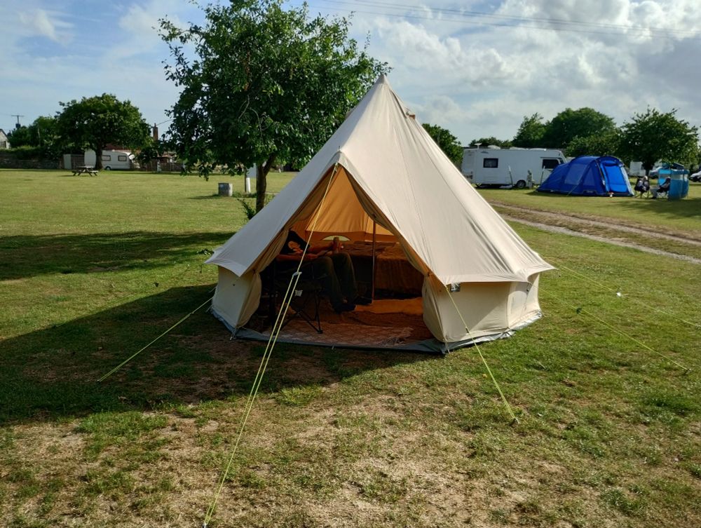 Our #belltent in an open, sunny campsite with small trees. More tents and some caravans in the background.