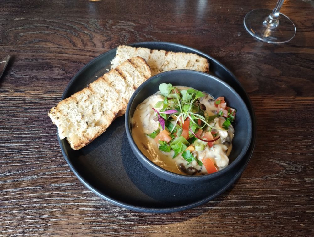 Grey plate with two fingers of focaccia  and a bowl of mushrooms in creamy sauce topped with microgreens and chopped tomato bits.