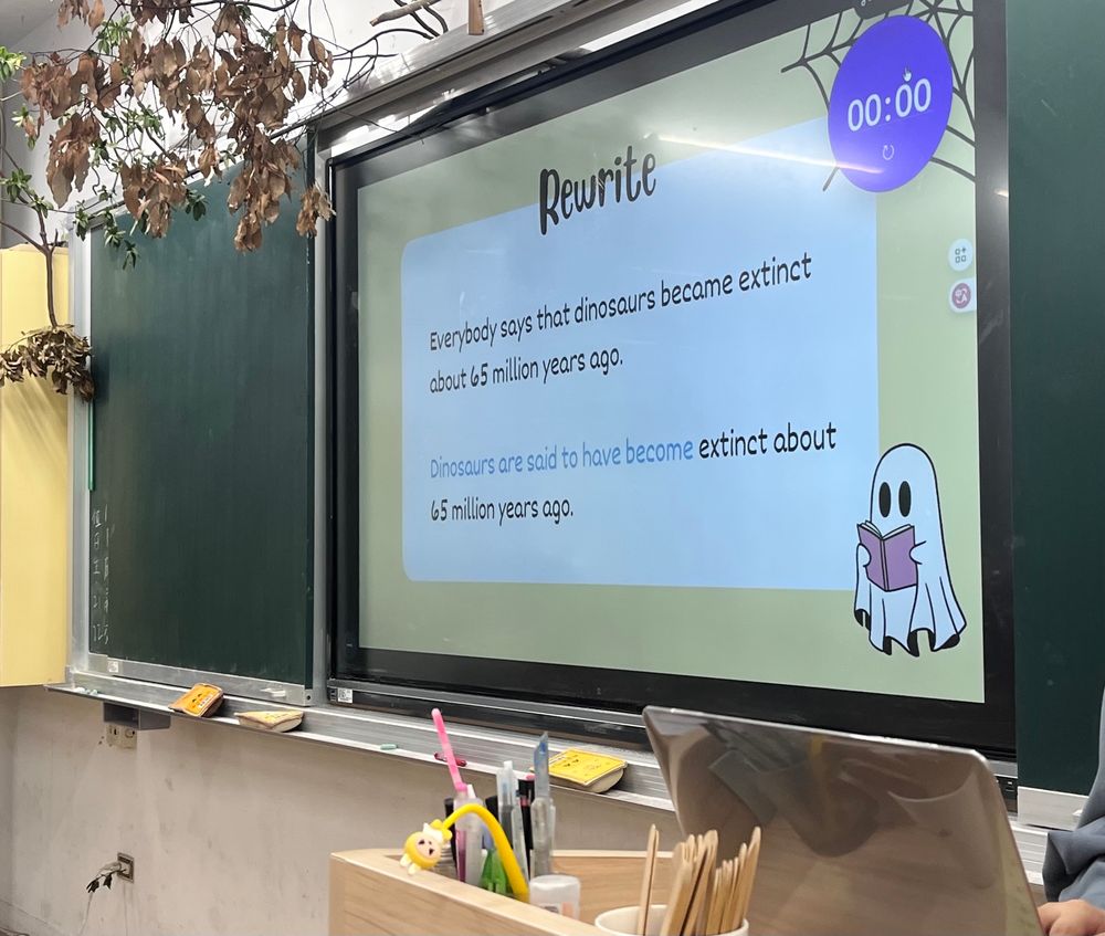 a page from a slide presentation saying: 
"Rewrite
Everybody says that dinosaurs became extinct about 65 million years ago.
Dinosaurs are said to have become extinct about 65 million years ago"
the page is projected onto a screen in a classroom.