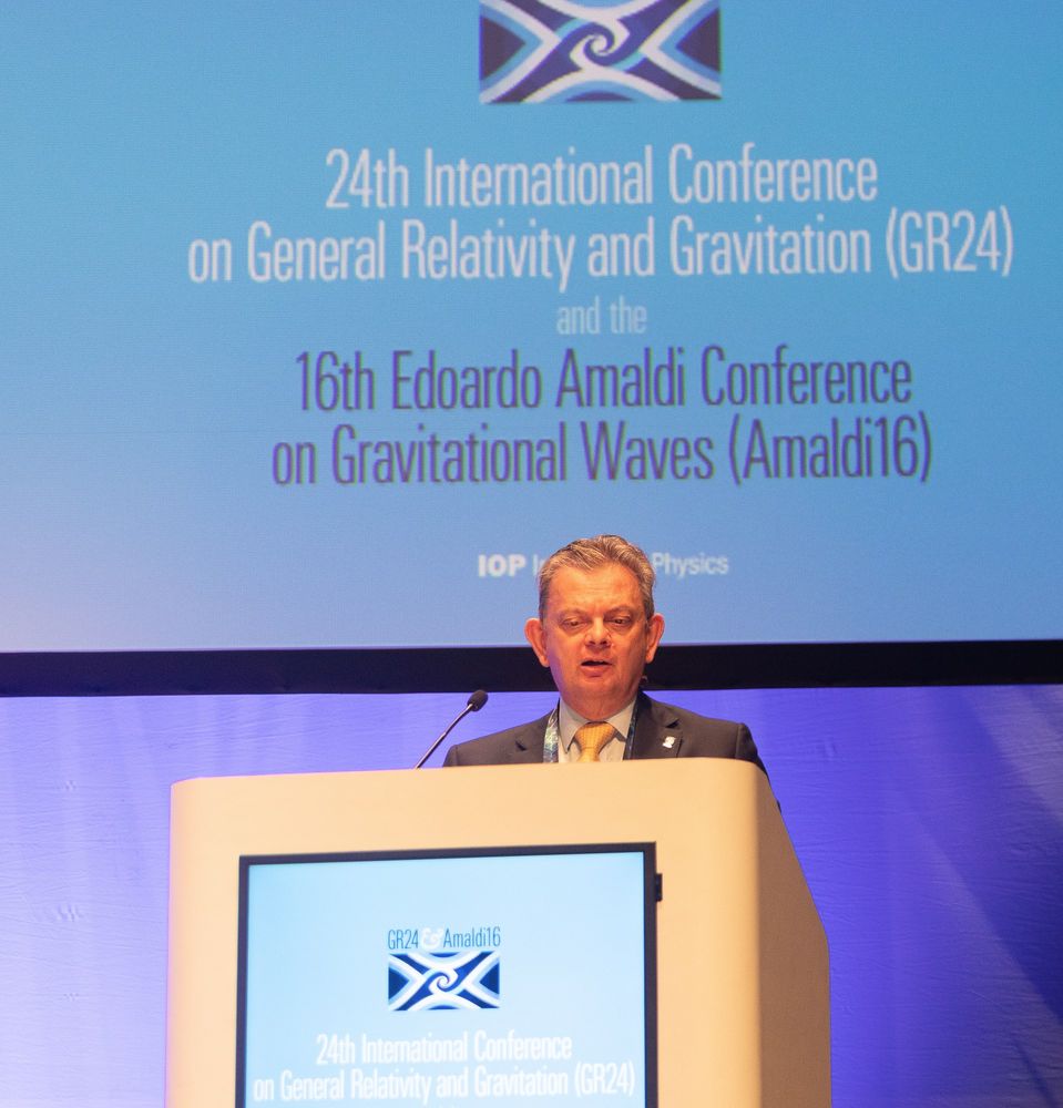 Professor Sir Anton Muscatelli FRSE standing at a rostrum speaking in front of a logo for the GR-Amaldi conference.