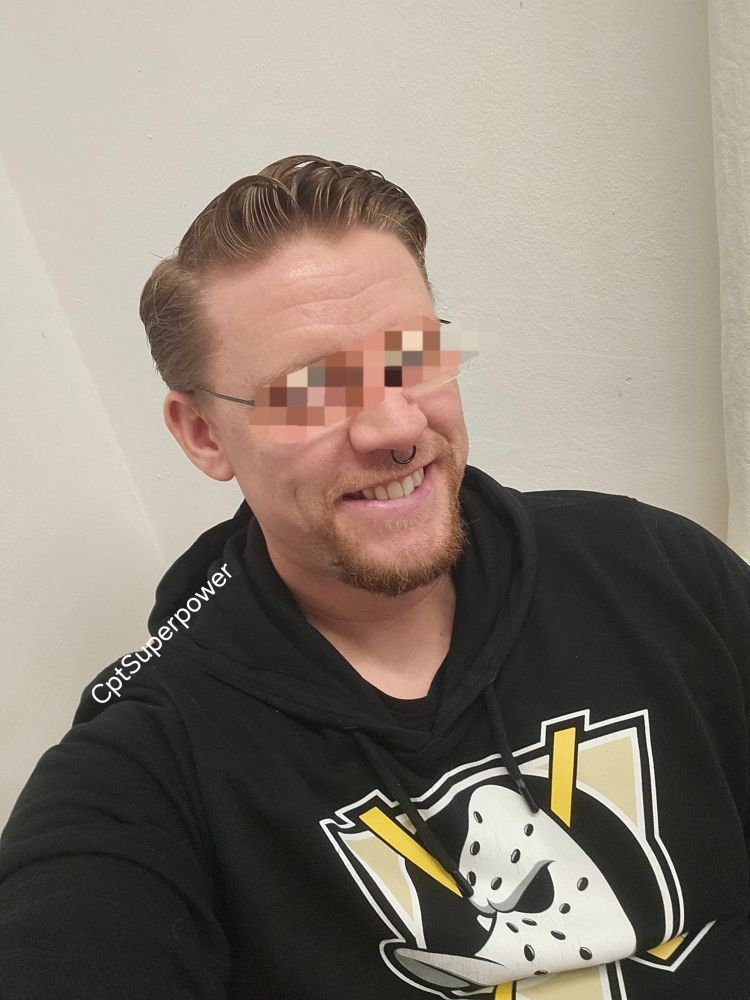 Ein Selfie von mir mit schwarzem Puli, auf dem eine Eishockeymaske in Form eines Entenkopfes ist