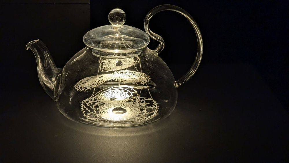A glass tea kettle with intricate lace made of paper in it.