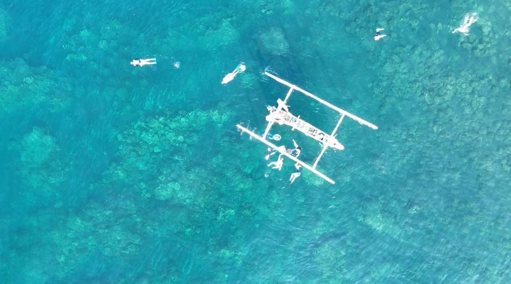 An overhead shot of the fishing boat and snorkelers, taking from a drone. 