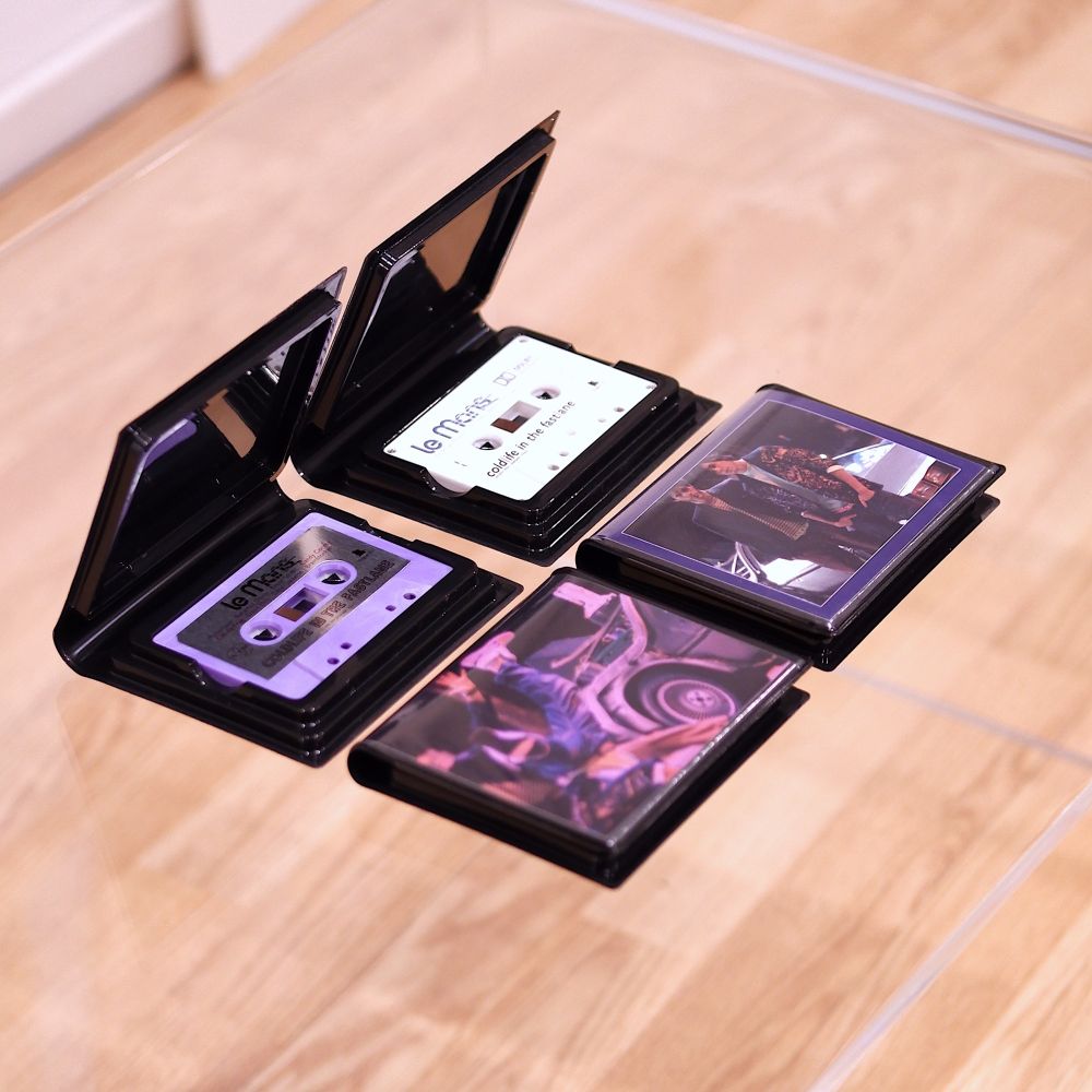 Photos of 20th anniversary cassette reissue of Le Mans' 2004 album, "Coldlife in the Fastlane" Each variant appears on a clear glass table sealed in a special drivers case (like a VHS cassette) and opened to show the actual physical media.

The Retrofit version features a swirled purple shell with one-sided silver foil label paying homage to the original 2004 magenta-washed design and adds an alternate behind the scenes image from the influential Delorean meets Miami Vice "time cops" photoshoot. 

The Deux Flics Dolby encoded variant features a Miami white cassette shell and cover art showcasing an alternate image of the two original band members in front of their DeLorean wearing Miami Vice meets electro fits from 2003 photoshoot often imitated in outrun and synthwave art.