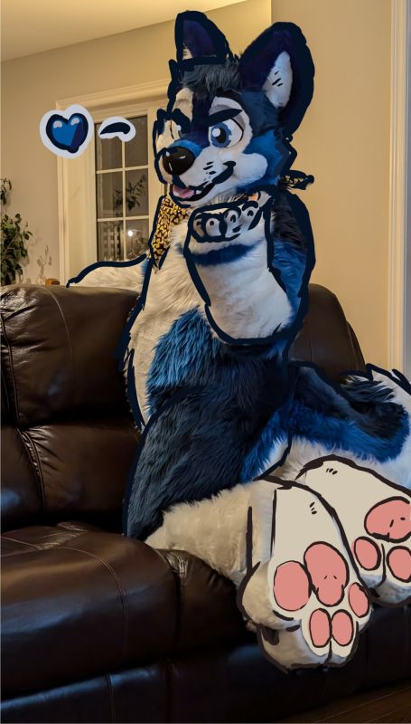 A drawover of Drake (in husky fursuit) kneeling on a couch while looking back towards the camera. He is blowing a kiss towards the viewer. The drawover stylizes his fur, face, and adds large pink pawpads to the soles of his hindpaws. A large blue heart is drawn out from his mouth.