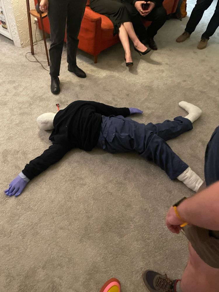 A white stunt dummy in trousers and a cardigan with an arrow sticking out of it splayed on the floor