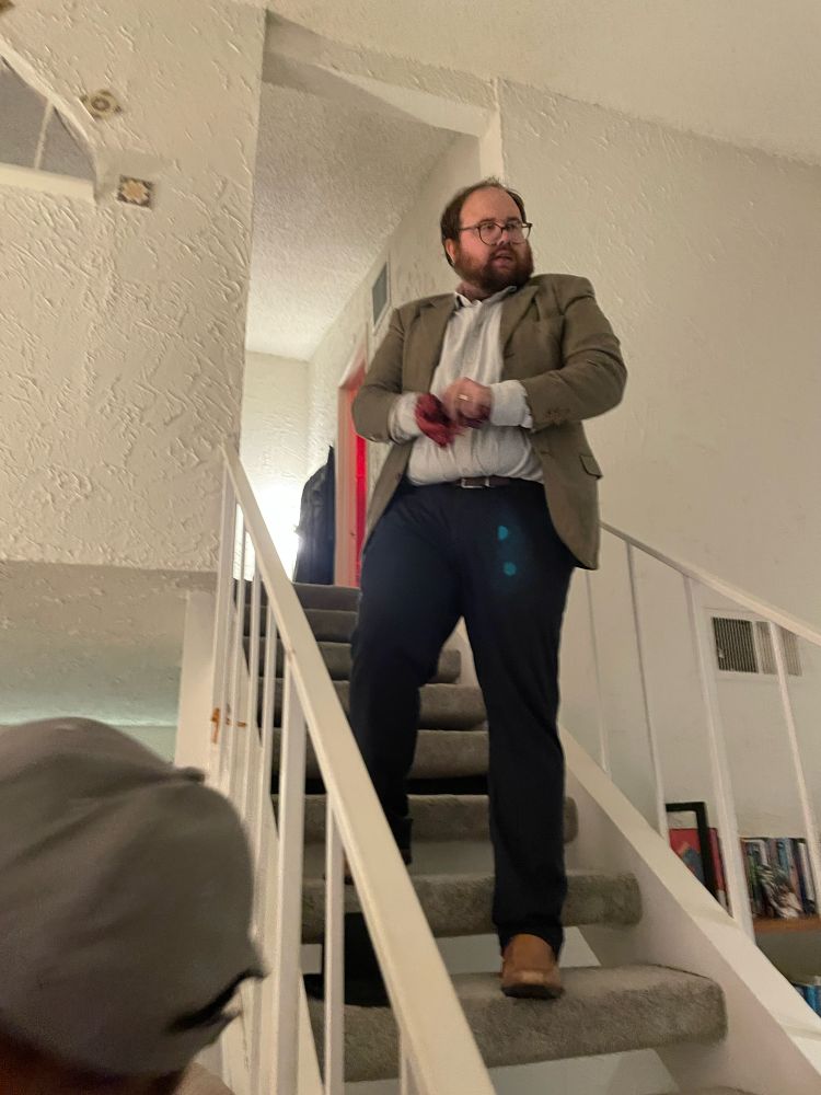 A man in a coat and bloody gloves standing on a staircase