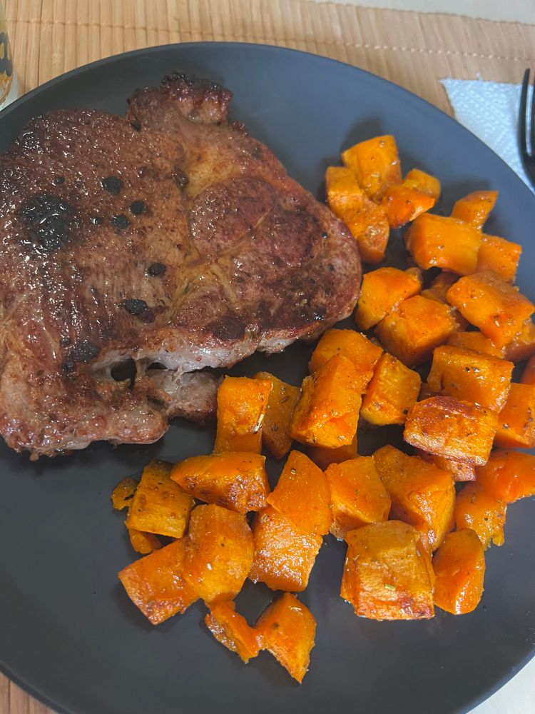 A picture of a marinated cut of pork with baked and seasoned sweet potatoes