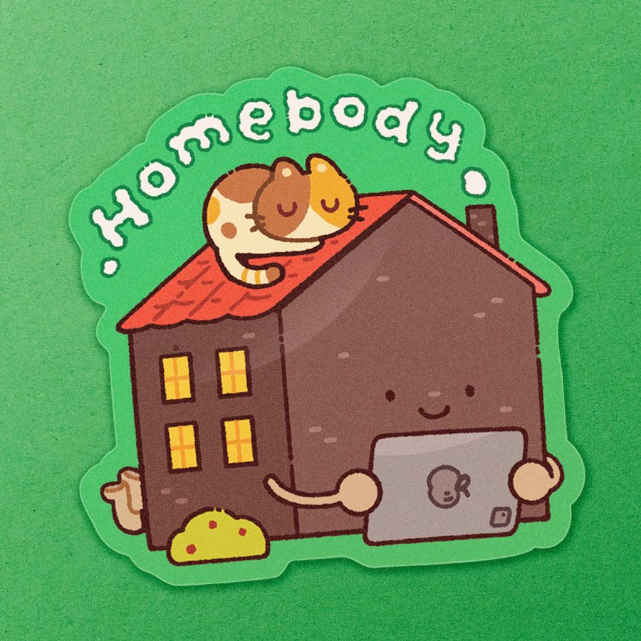 Die-cut vinyl depicting an anthropomorphic house resting on their tummy, holding an iPad and kicking their feet. A calico cat is sleeping on the roof. Puffs of smoke is blowing out of the chimney, spelling the word "Homebody".