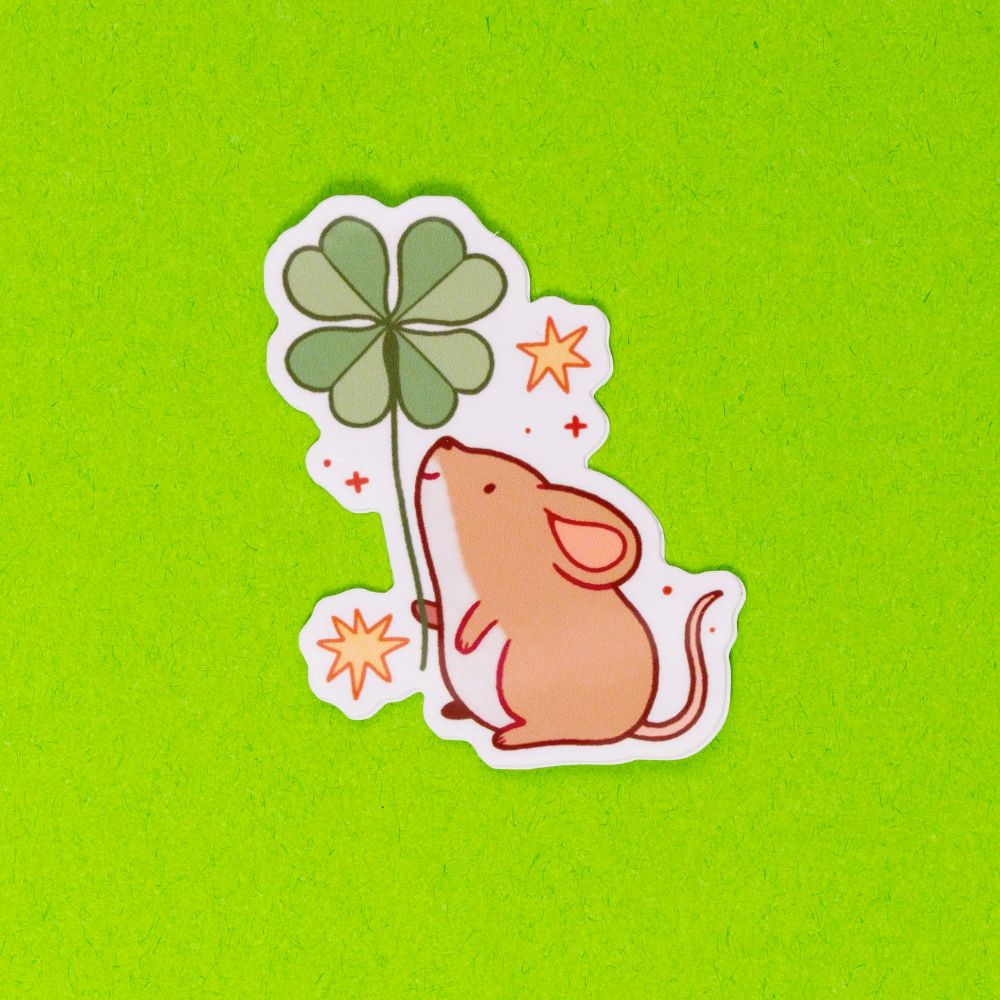 A die-cut vinyl sticker of a short, round mouse holding a four-leaf clover while surrounded by stars.