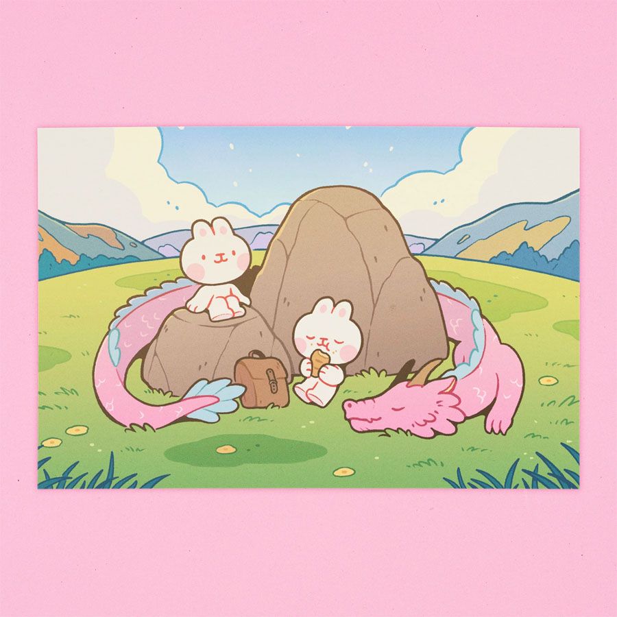 Art print depicting two bunnies having a snack break in a rocky part of a grassy field. A pink dragon curls up around the rocks, napping.