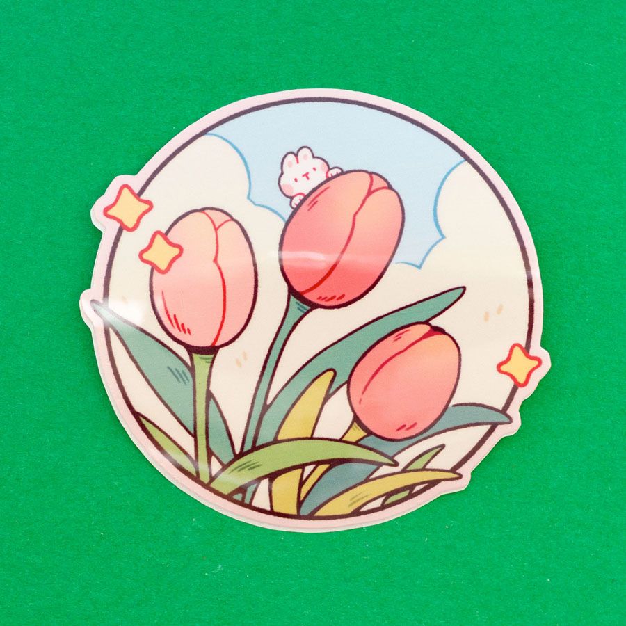 A single die-cut vinyl sticker depicting a bunch of pink tulips against a cloudy sky. There is a tiny bunny peeking from behind one of the buds.