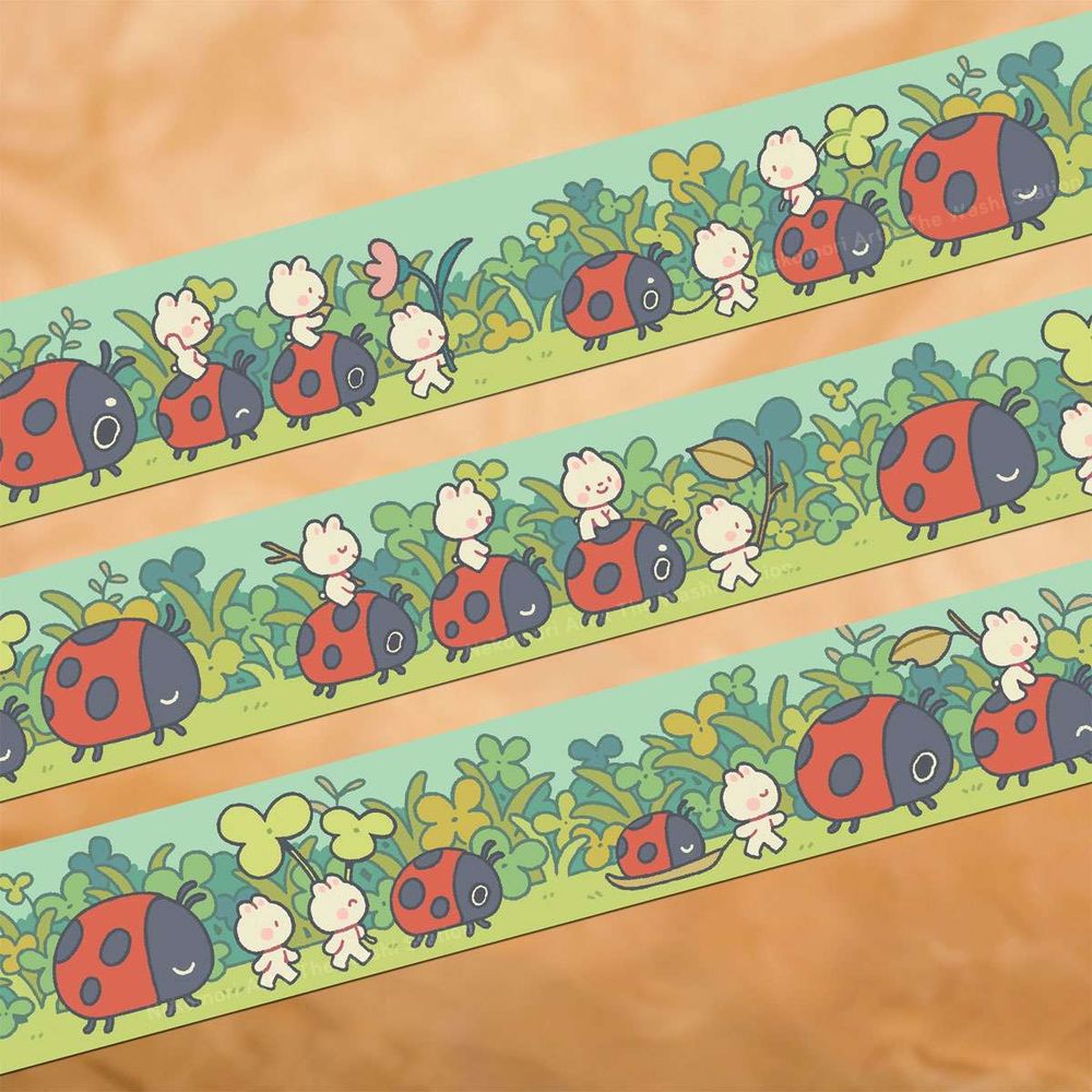 Mock up of a washi tape called "Ladybug March", designed by Nekomori Art for The Washi Station. It depicts groups of ladybugs and tiny bunnies marching through a field against a backdrop of clovers and grass. Some of the bunnies are walking with a twig or a flower in hand, others are riding on the ladybugs or otherwise guiding them along. They all look excited to head to their destination.
