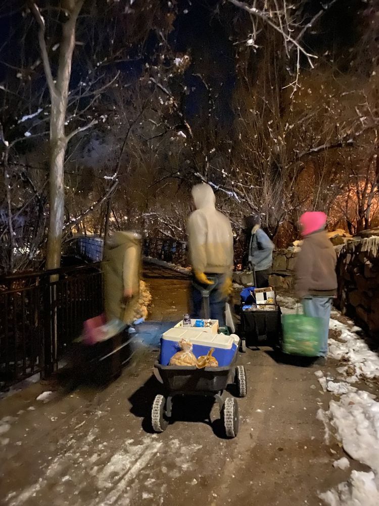 A photo of four blurry figures in the snow carrying wagon's and bags full of supplies.