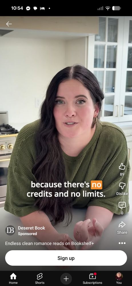 White woman with long dark brown hair in a green shirt leaning on a kitchen counter with a stove and cabinet behind her. 