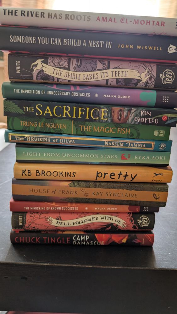 It's a book stack starting at the top: The river has roots by Amal El mortar Someone you can build a nest in. John Wiswell The spirit bears its teeth by Andrew Joseph White The imposition of unnecessary obstacles by malka older The sacrifice by Ryn chapeco The magic fish by Trung Le Nguyen The bruising of kilawa by, Naseem jamnia Light from uncommon Stars by Ryka Aoki Pretty by KB Perkins House of Frank by Kay Sinclair The mimicking of known successes by Malka Older hell followed with us by Andrew Joseph White camp Damascus by Chuck tingle