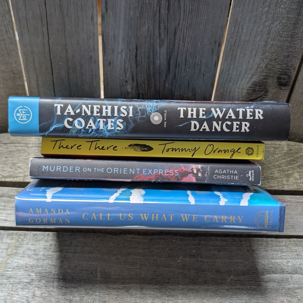 A stack of 4 books on a wood background 
Top down
Ta-nehisi Coates the water dancer
There, there Tommy orange
Murder on the Orient Express, Agatha Christie 
Call us what we carry, Amanda Gorman