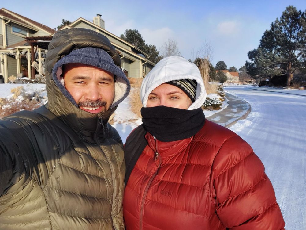 Jess and her husband in puffy jackets all bundled up standing on the snow covered street 