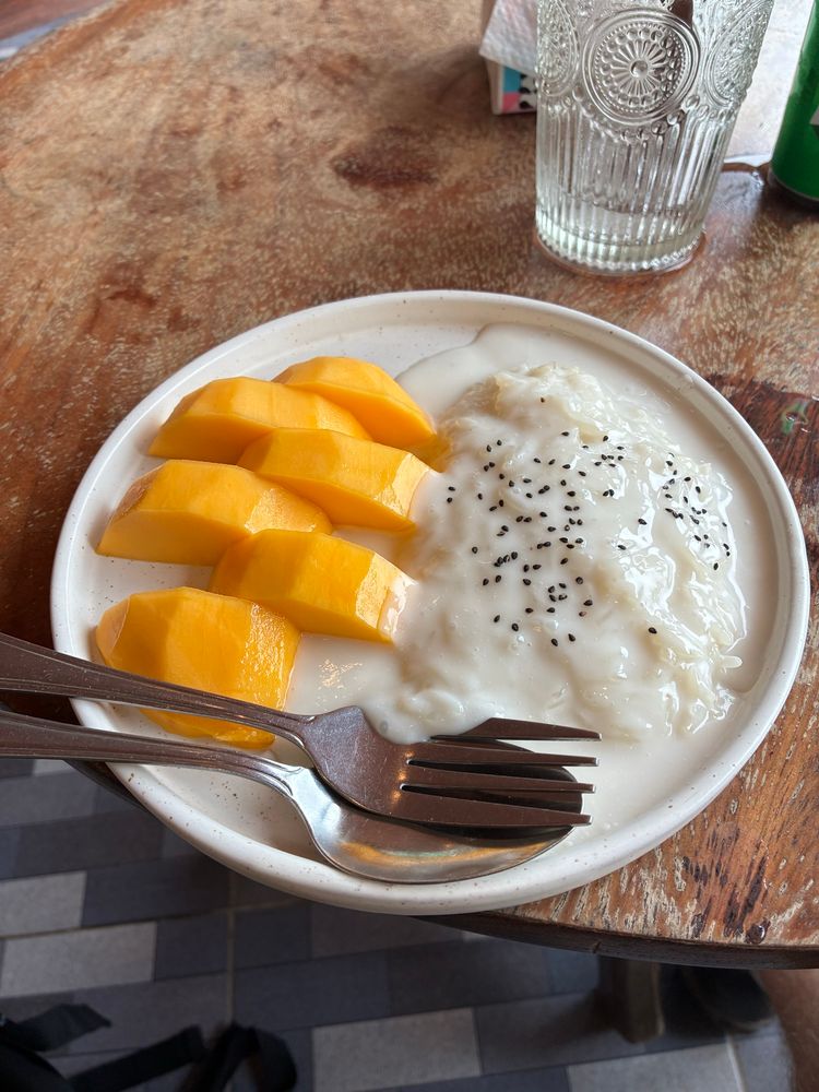 Ein Teller mit einer Portion Mango Sticky Reis und besteck auf einem Holztisch.