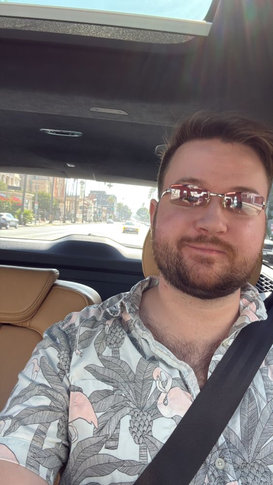 Lucas in an Uber wearing a Hawaiian shirt that’s partially unbuttoned and wearing some y2k sunglasses