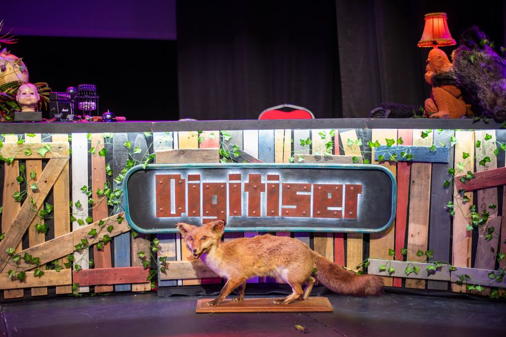 Digitiser Live 2019 desk, with the Digitiser logo on the front - wood panelling on the front as well, and a fake fox in front of it. 