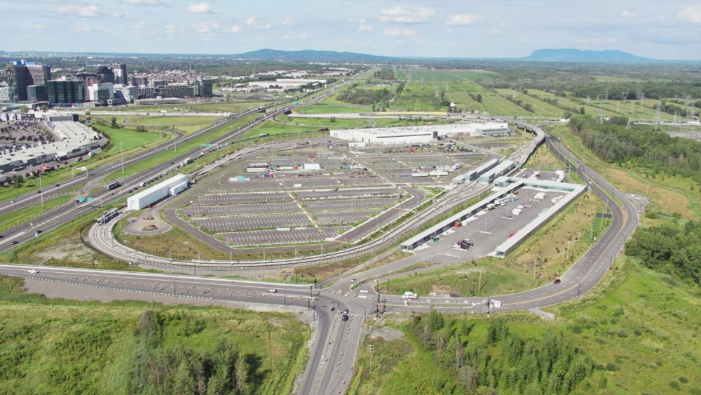 Brossard station, on the Réseau express métropolitain (REM) in Montreal and its suburbs. The train station is a tiny building attached to a giant bus terminal attached to a truly vast parking lot. The image is 60% parking lot, 35% green space, and about 5% combined bus and train station. wild!