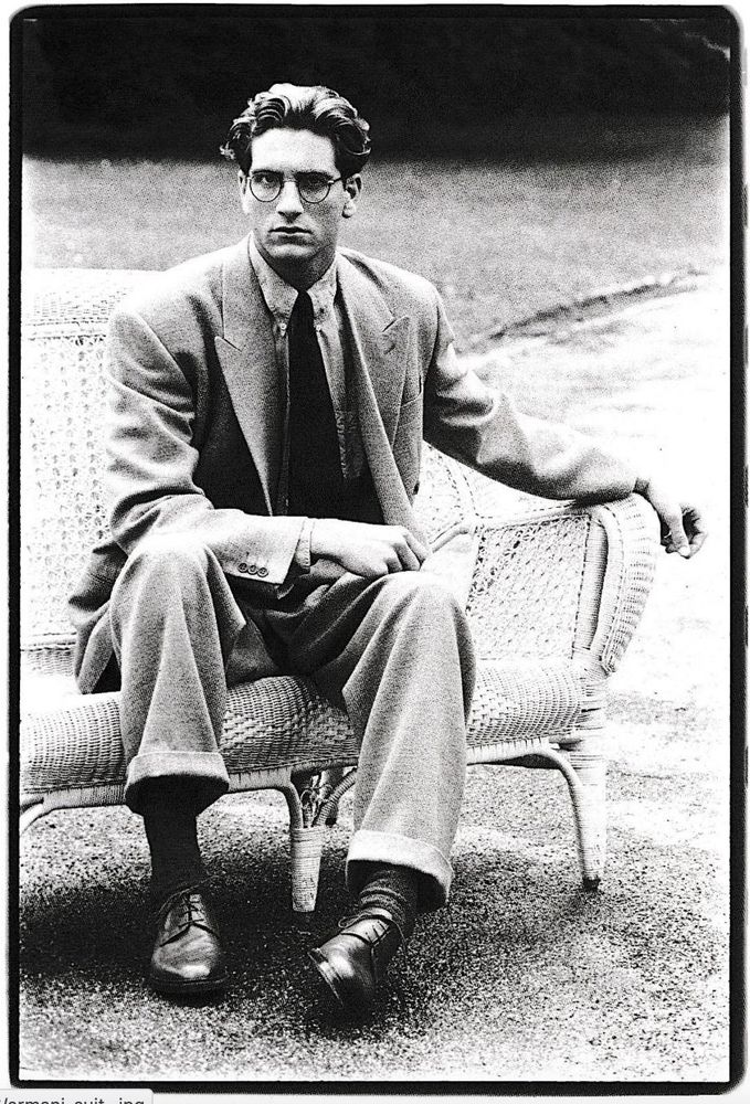 Svartvit bild på man i dubbelknäppt Armanikostym sittande på en rottingsoffa.