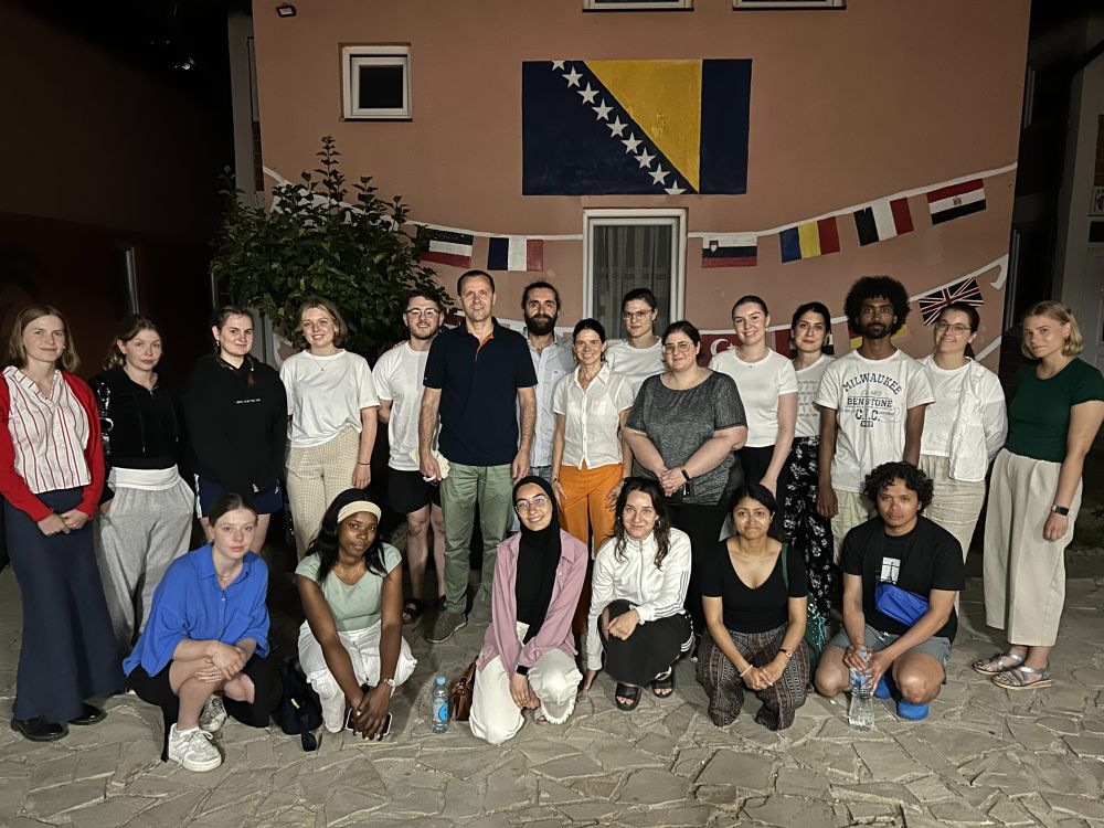 Students who participated in the study trip pose together in front of a wall showing different flags.
