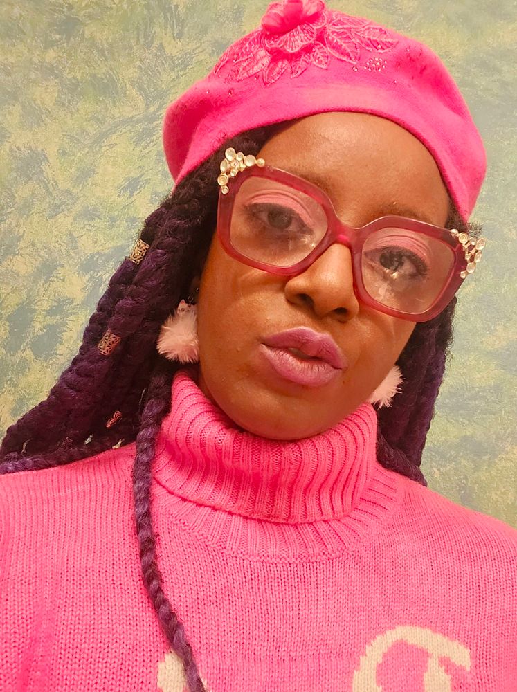 African American women in a pink turtleneck, hat, and puffy pink earrings.