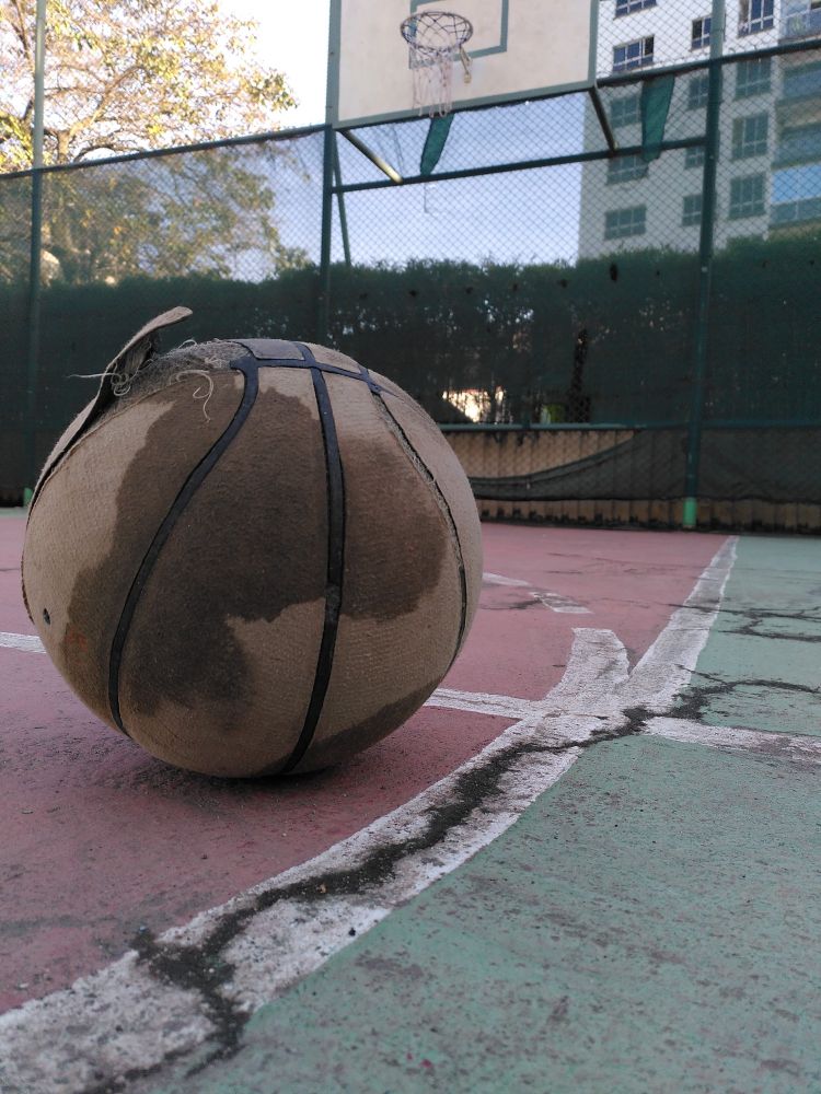 Old basketball on cracked court in front of basketball hoop in Nairobi.