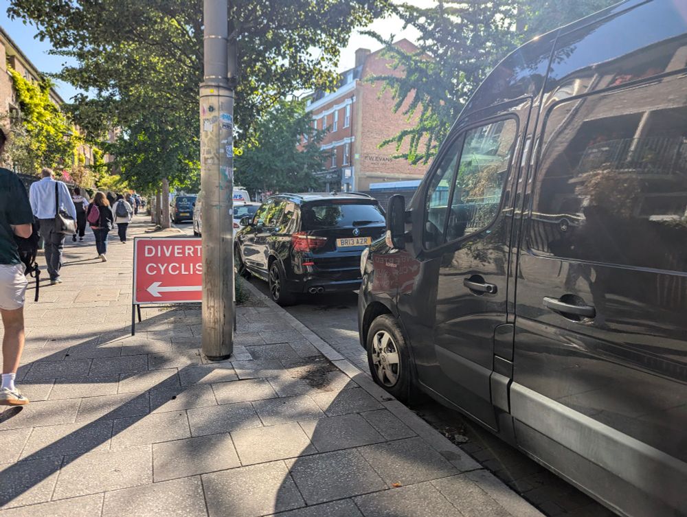 Sign that says diverted cyclists obscured by a lampost and parked van