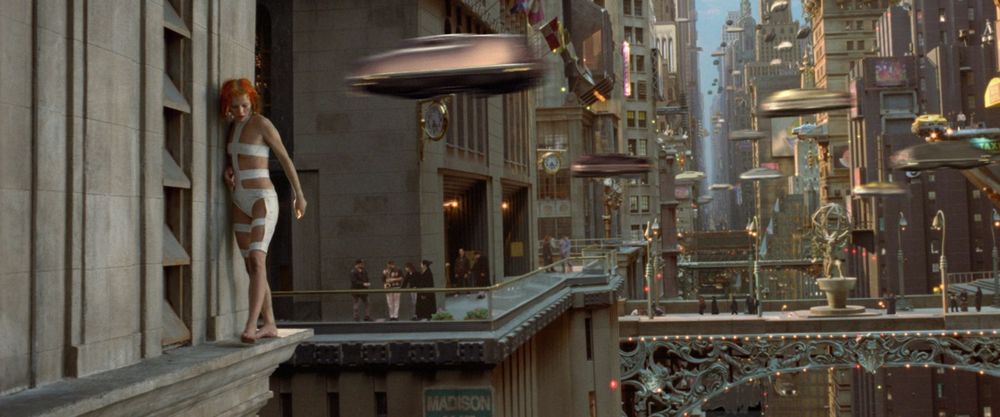 A futuristic cityscape with flying vehicles and a young woman, Leeloo. The city is densely populated with towering buildings and intricate bridges. The woman, dressed in a white outfit, appears to be looking out at the bustling scene below.