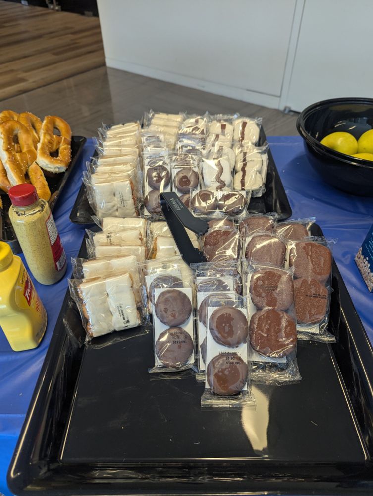 A catering table with a blue tablecloth that features three kinds of Tastykakes and Philadelphia-style pretzels (with mustard)
