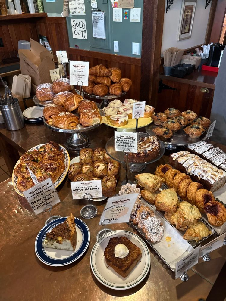 A corner counter covered in plates and trays, each filled with danishes, scones, biscuits, croissants, muffins, and other pastries