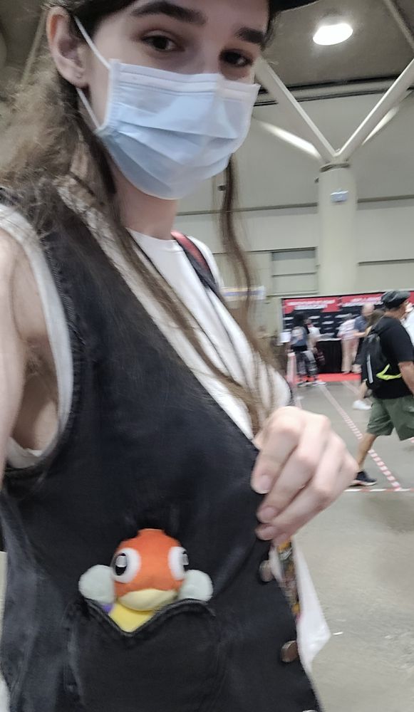 emily at the con with a mask on, and a ledyba plush peeking out of her pocket!