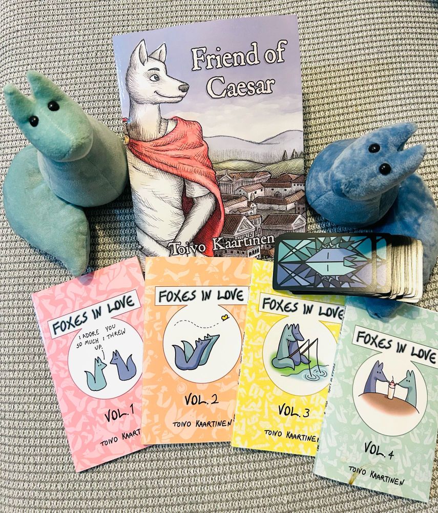 My own collection of the Foxes In Love merch produced by Fenris Publishing: 4 albums of Foxes In Love comics, the first book of Toivo Kaartinen’s unrelated series Friend of Caesar, a pack of Foxes in Love tarot deck, and Green and Blue fox plushies.
